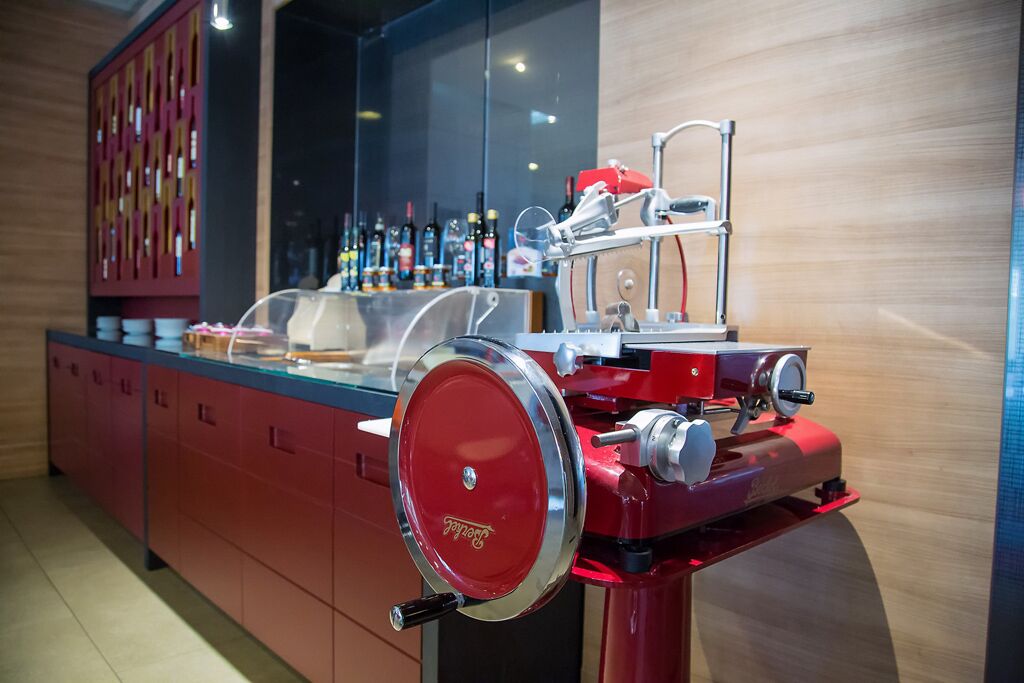 Zona de bar con un mostrador rojo, una vitrina de vidrio y una variedad de botellas al fondo.