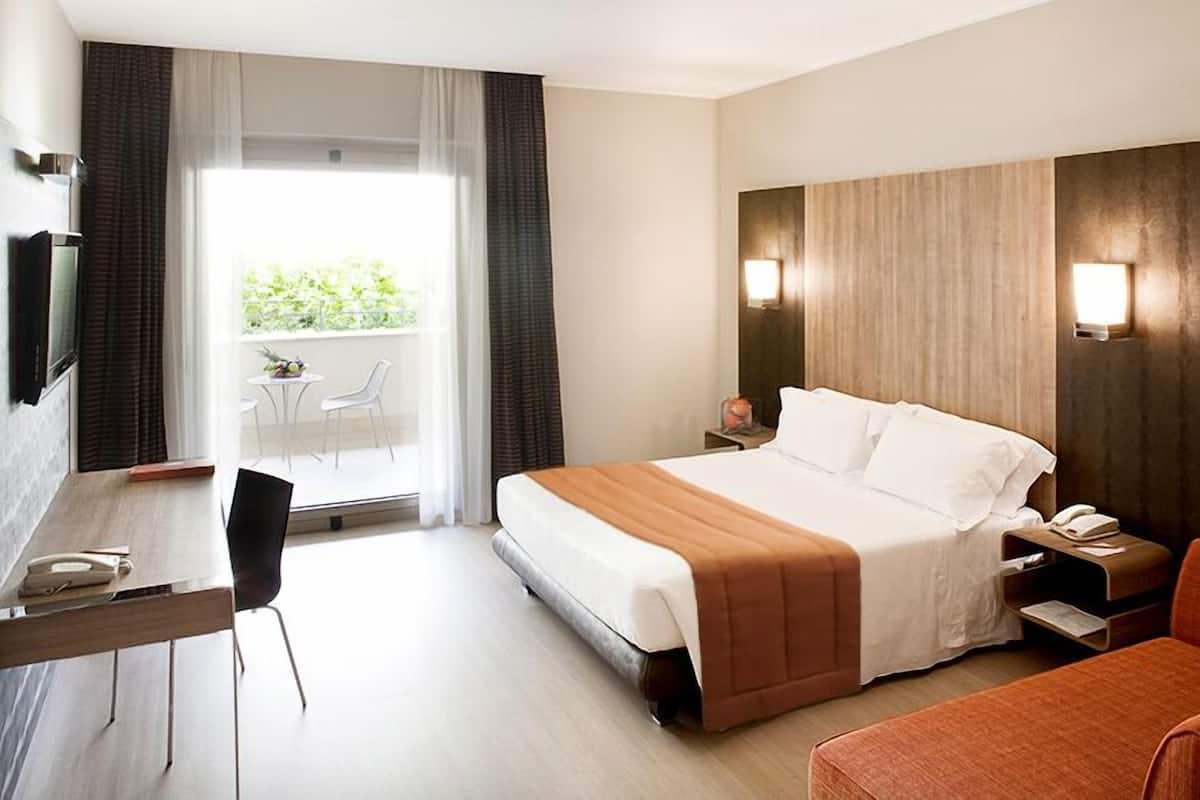 Een hotelkamer met een bed, een bureau, een stoel, een nachtkastje en uitzicht op de omgeving.