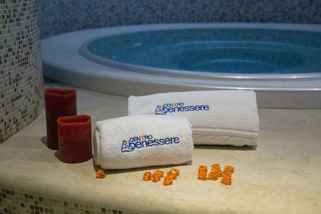 Une salle de bain avec une baignoire, deux serviettes blanches et une bougie rouge.