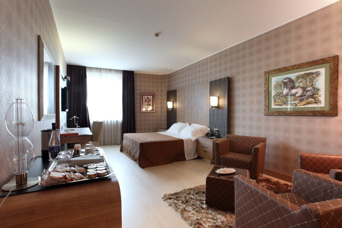 Een hotelkamer met een bed, een bank, een bureau met lamp, een televisie en een dienblad met ontbijtartikelen.