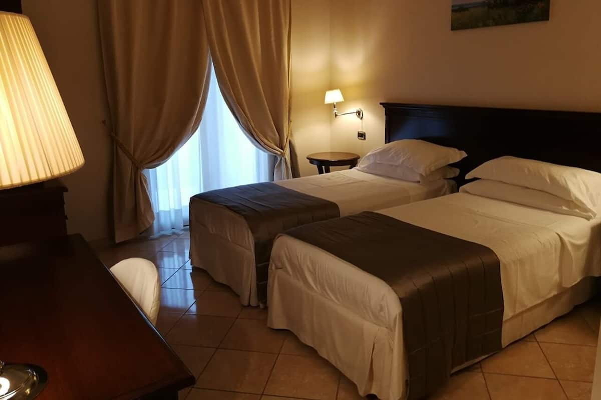 Ein Hotelzimmer mit zwei Betten, einem Schreibtisch, einer Lampe und einem Fenster mit Vorhängen.