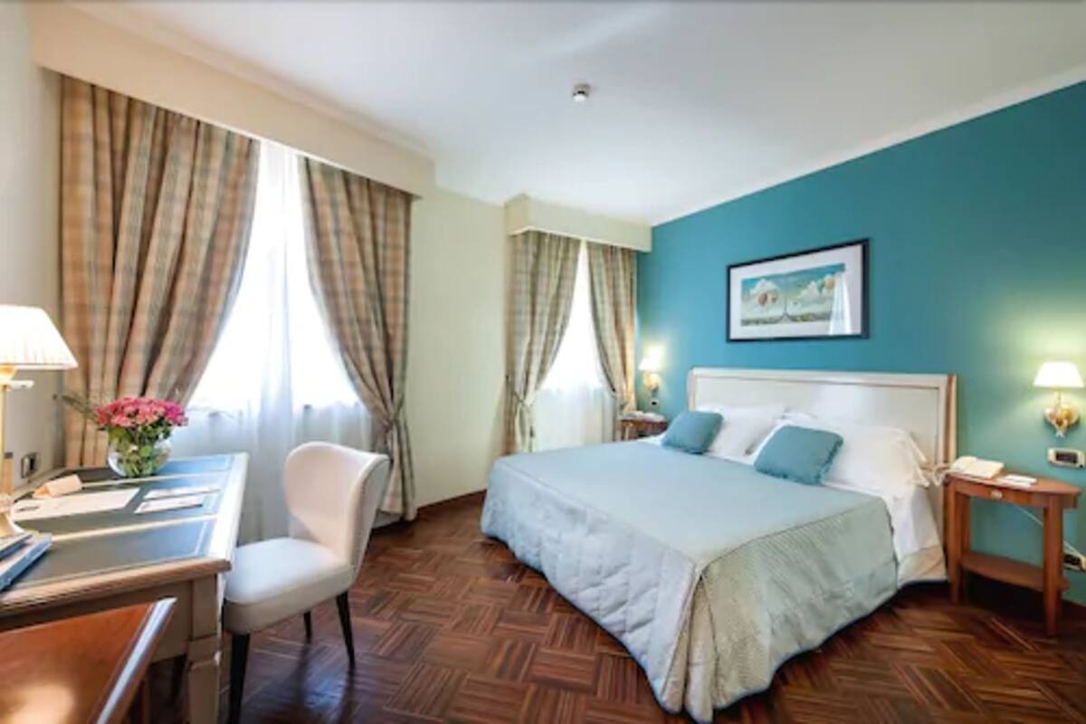 Ein Hotelzimmer mit Bett, Schreibtisch, Stuhl und einem Vorhangfenster.
