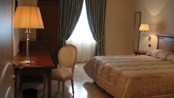 A hotel room with a bed, a desk with a lamp, a chair, and a window with curtains.