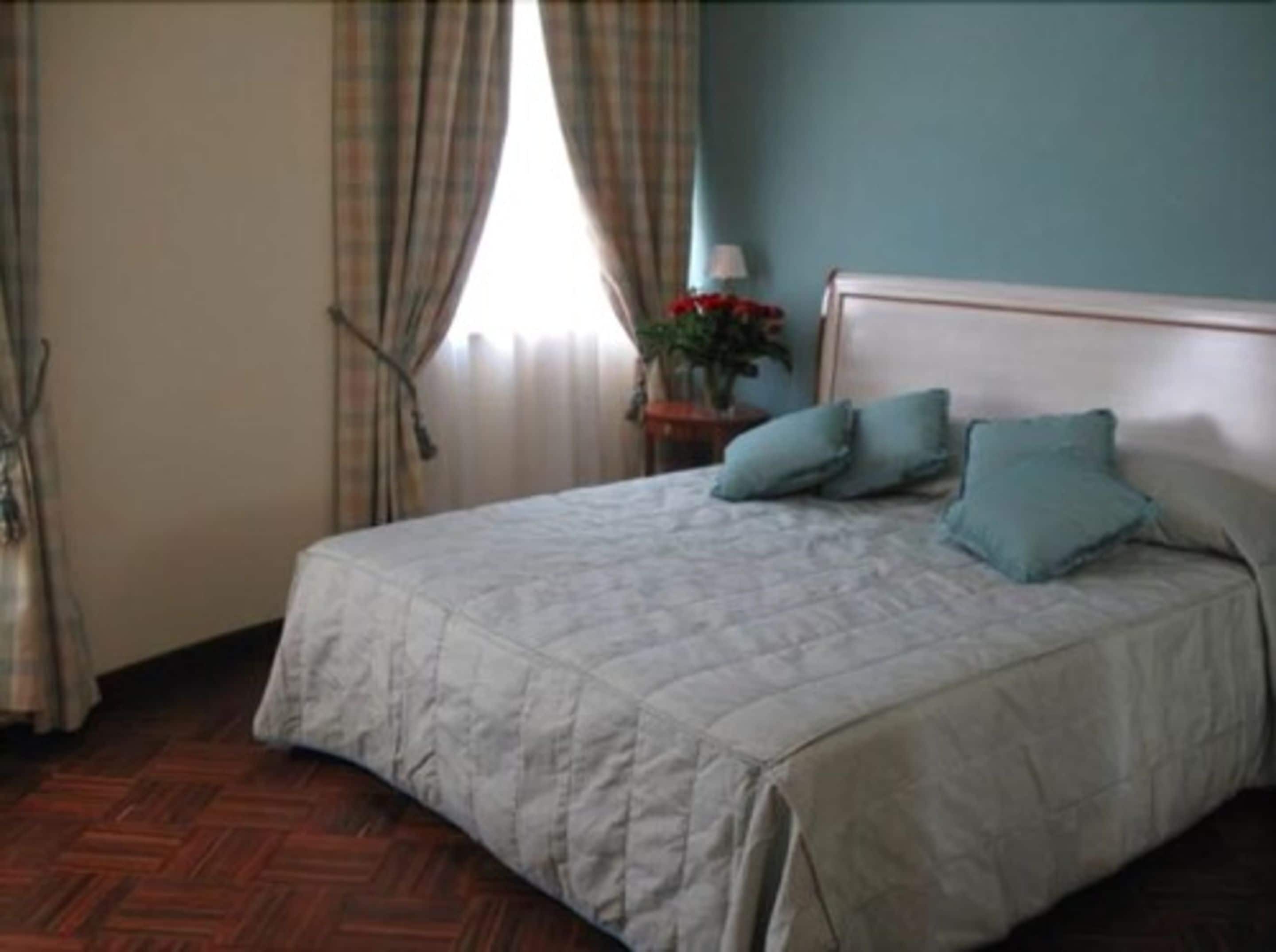 Un dormitorio con cama, mesita de noche, lámpara y ventana con cortinas.