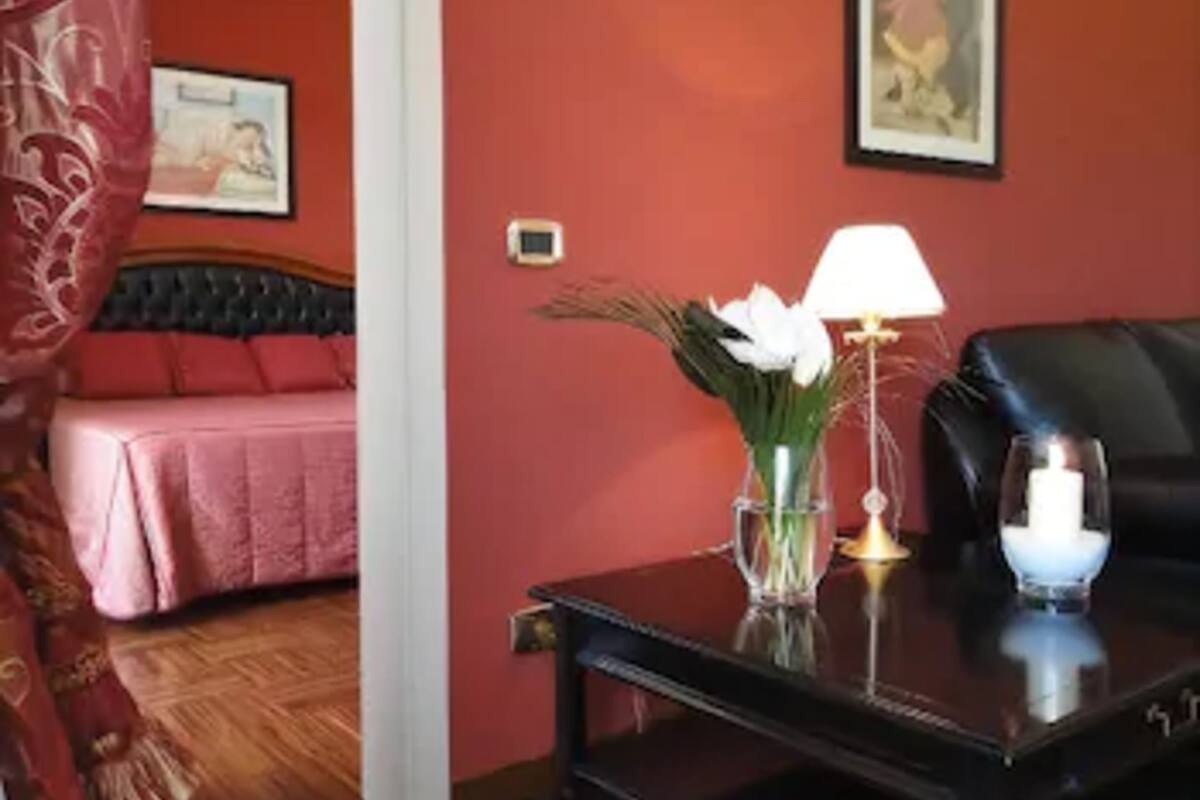Ein Zimmer mit einem Bett, einem Tisch mit Blumenvase, einer Lampe und einer Kerze.
