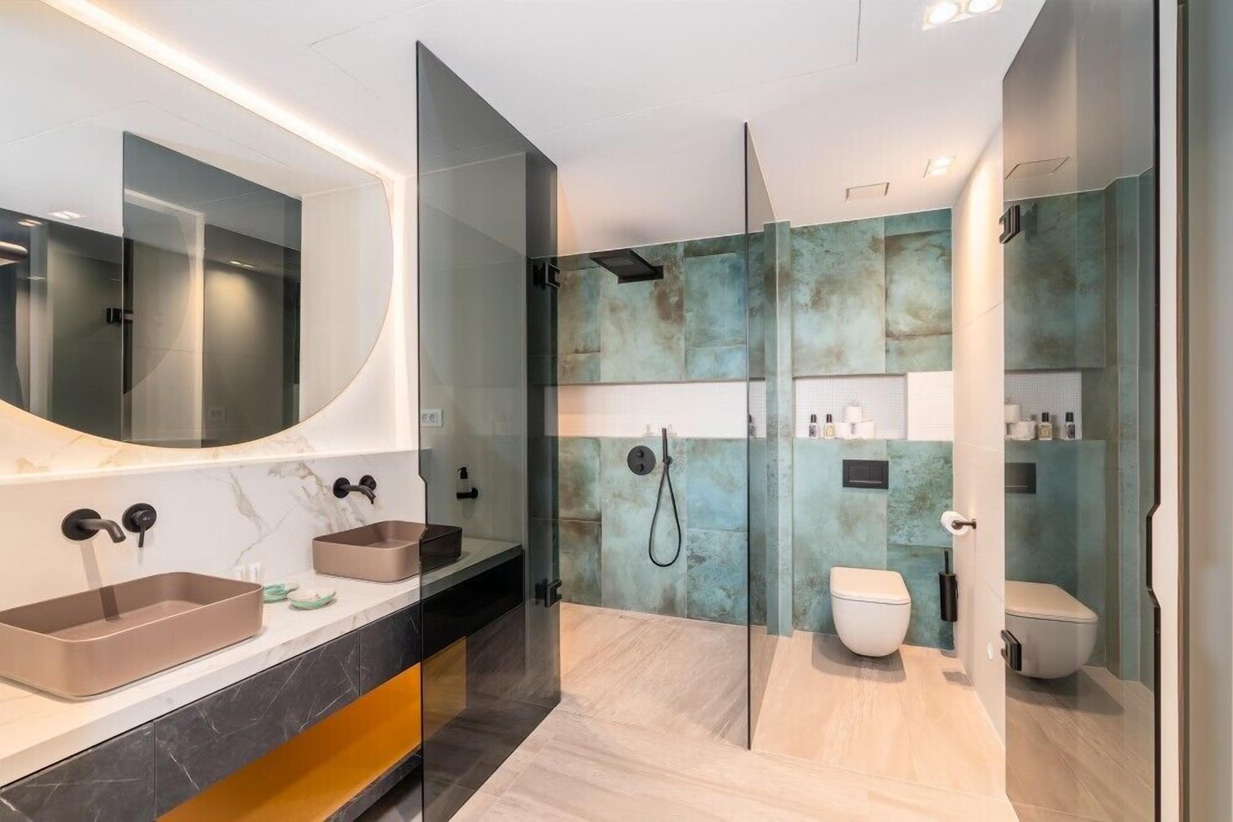 A modern bathroom with a large mirror, two sinks, a shower, and a toilet.