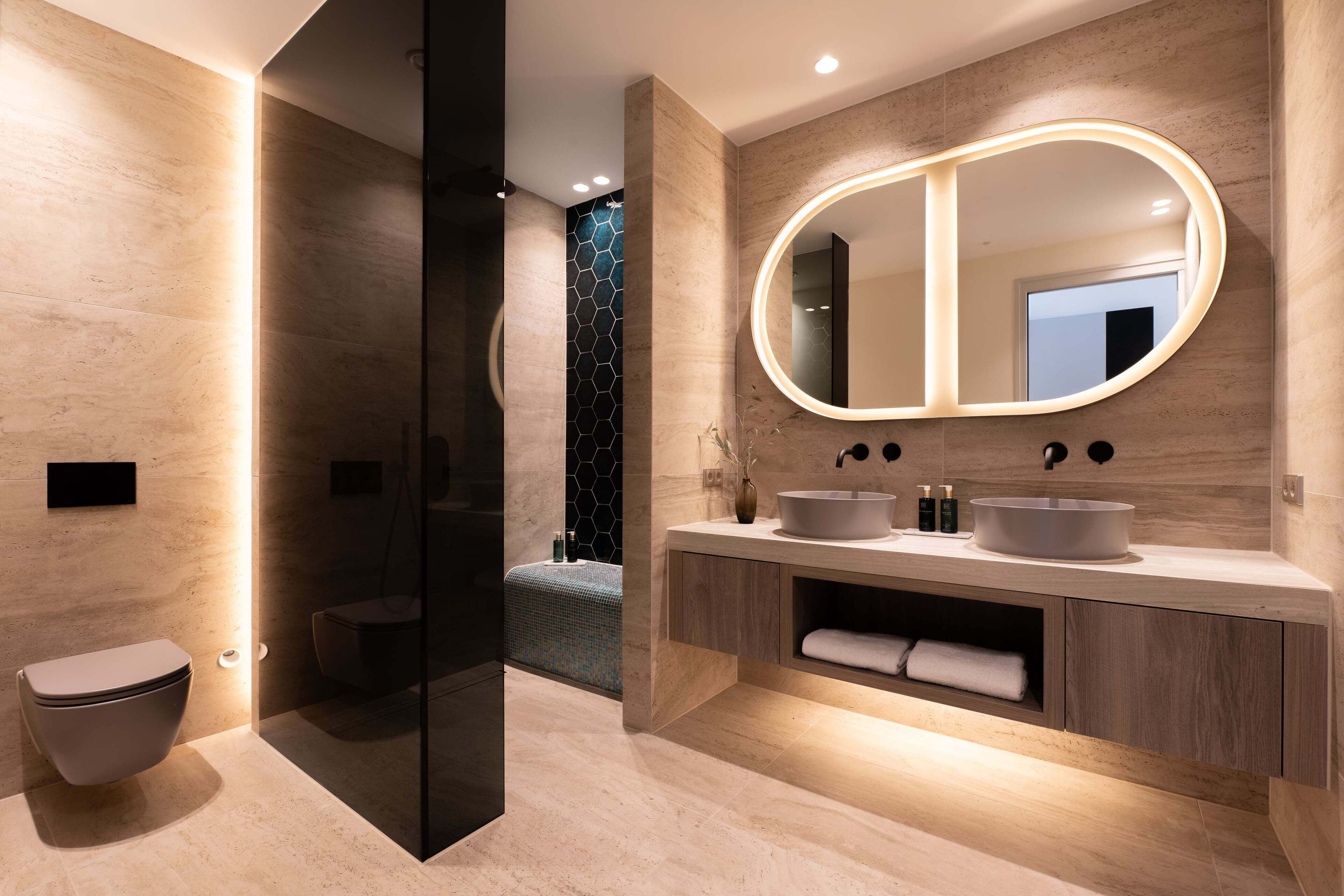 A modern bathroom with a large mirror, two sinks, and a toilet.