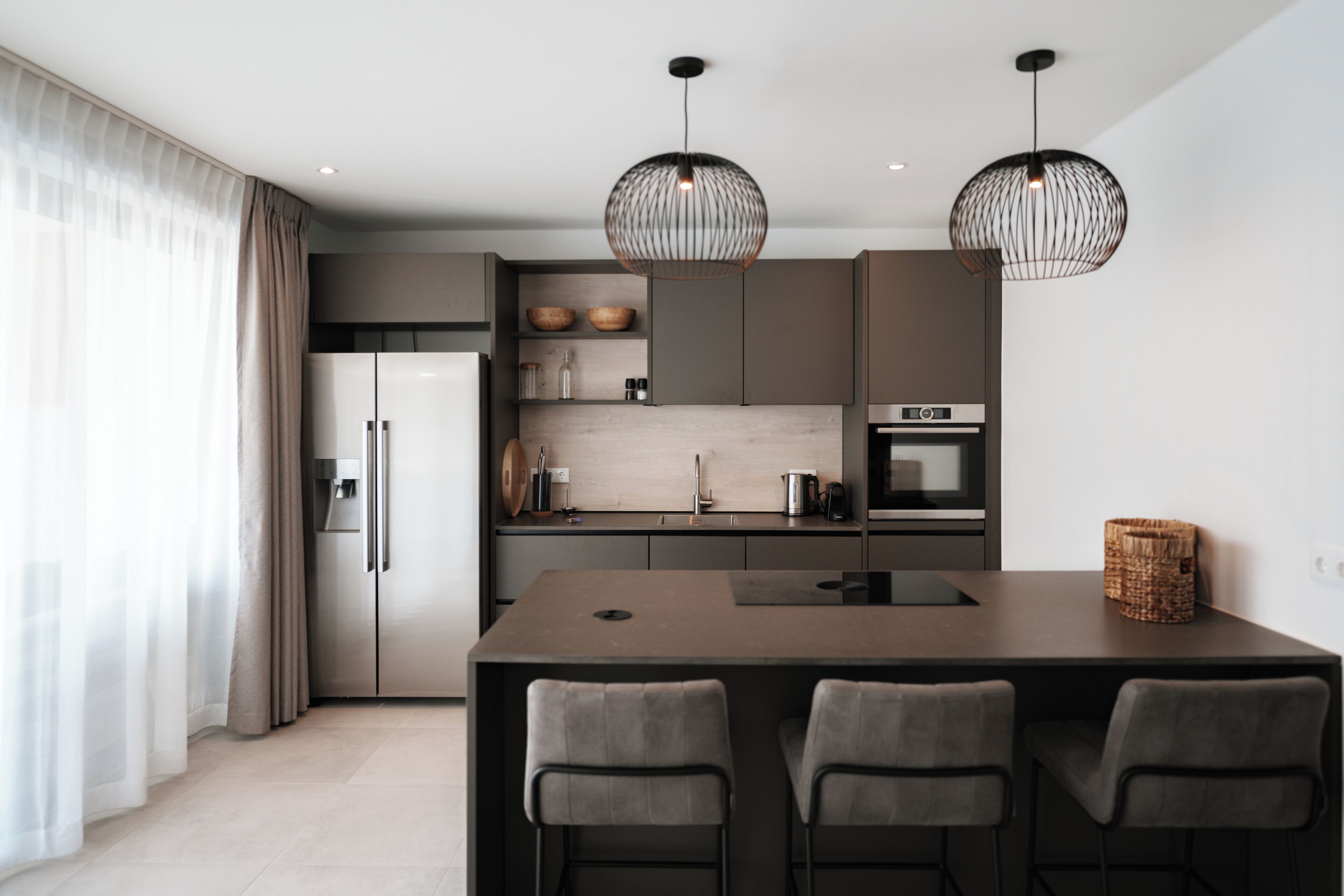 Una cucina moderna con isola centrale, due lampade a sospensione e un frigorifero.