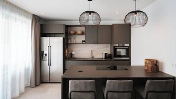 Una cucina moderna con isola centrale, due lampade a sospensione e un frigorifero.