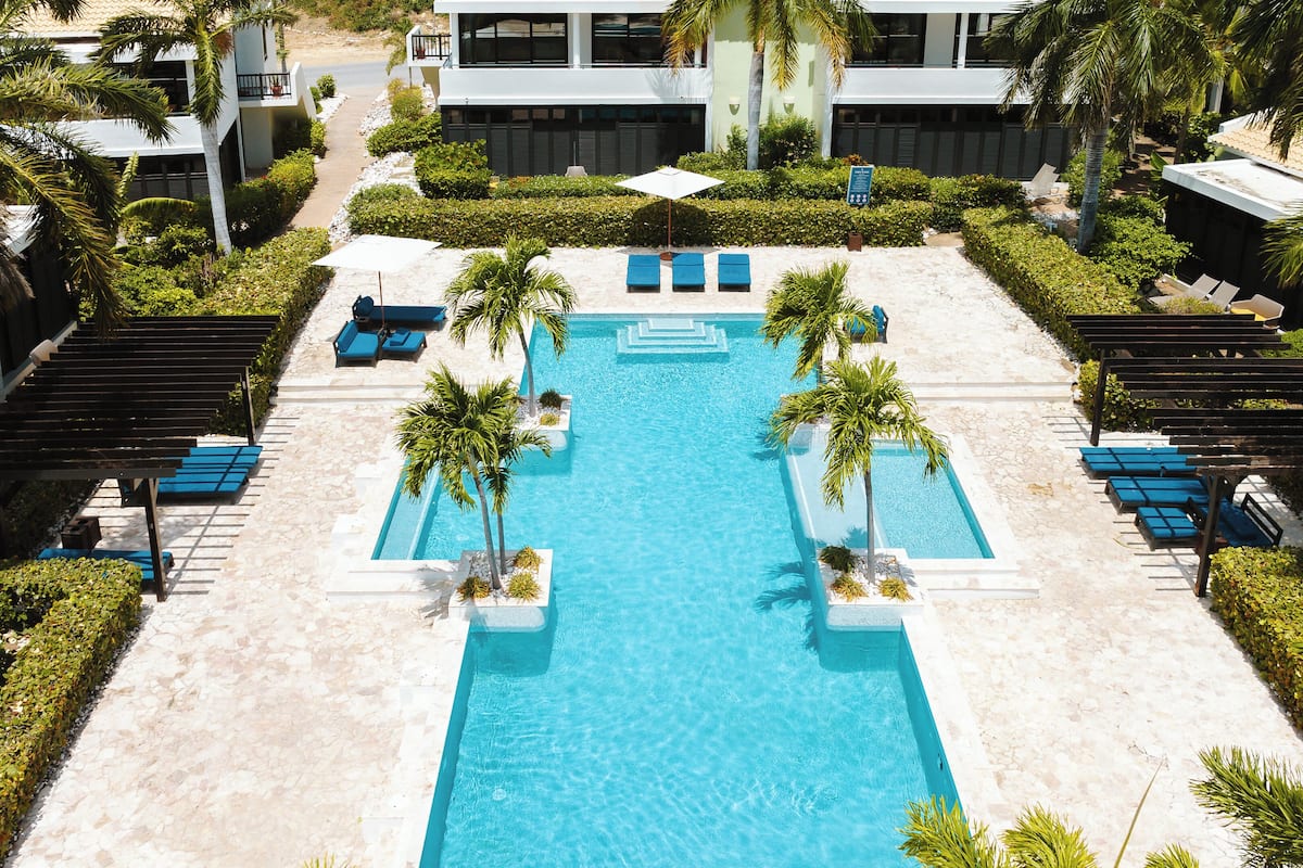 Un espace piscine avec une eau d’un bleu limpide, entouré de chaises longues et de palmiers.