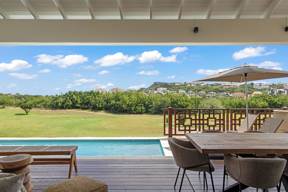 A poolside area with a wooden deck, outdoor furniture, and a view of a residential area.