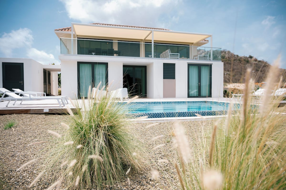 Une maison moderne à deux étages, dotée d’une piscine, d’un patio couvert et offrant une vue sur le paysage environnant.