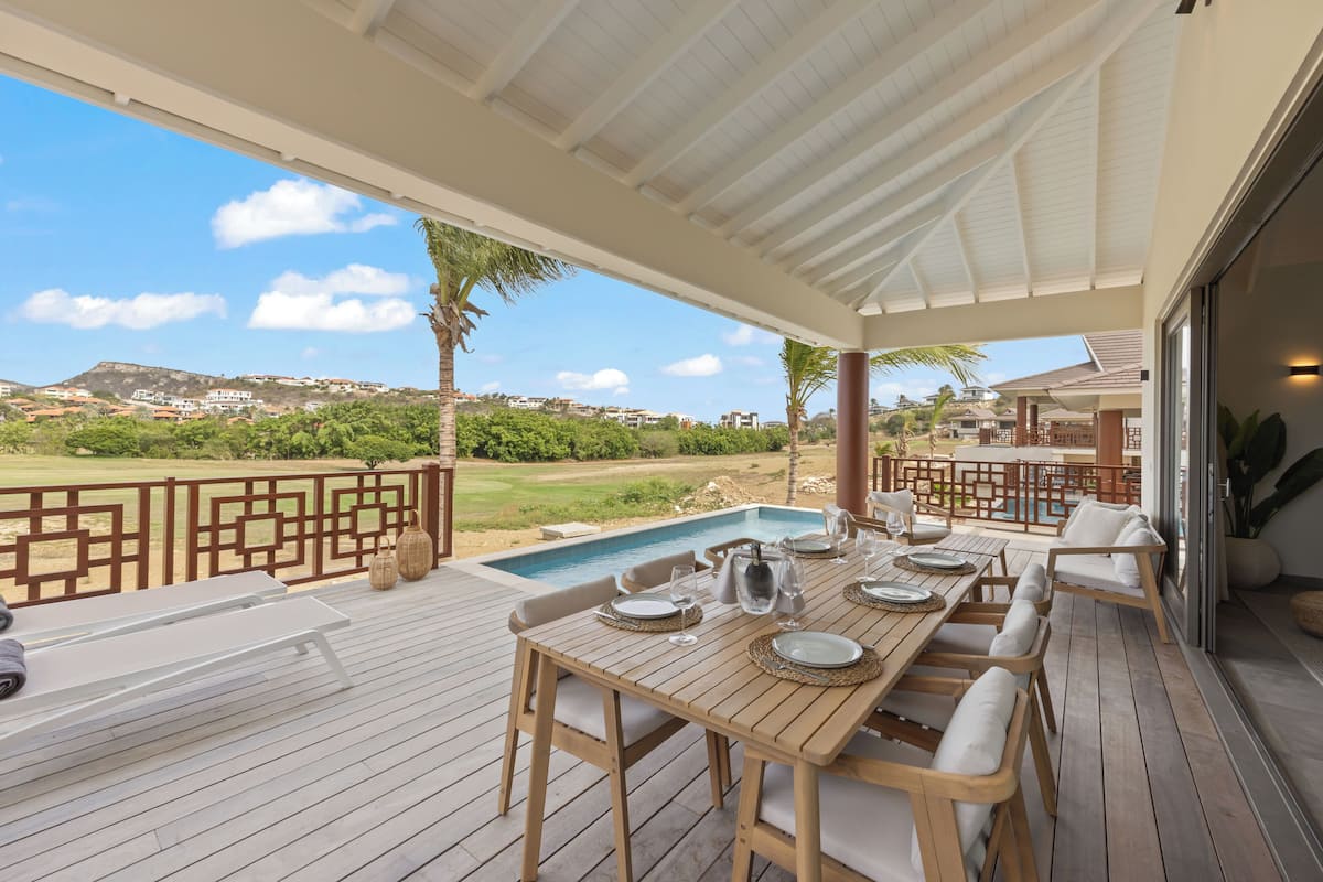 Un espace extérieur abrité, aménagé pour les repas, avec une piscine, du mobilier en bois et une vue sur le paysage environnant.