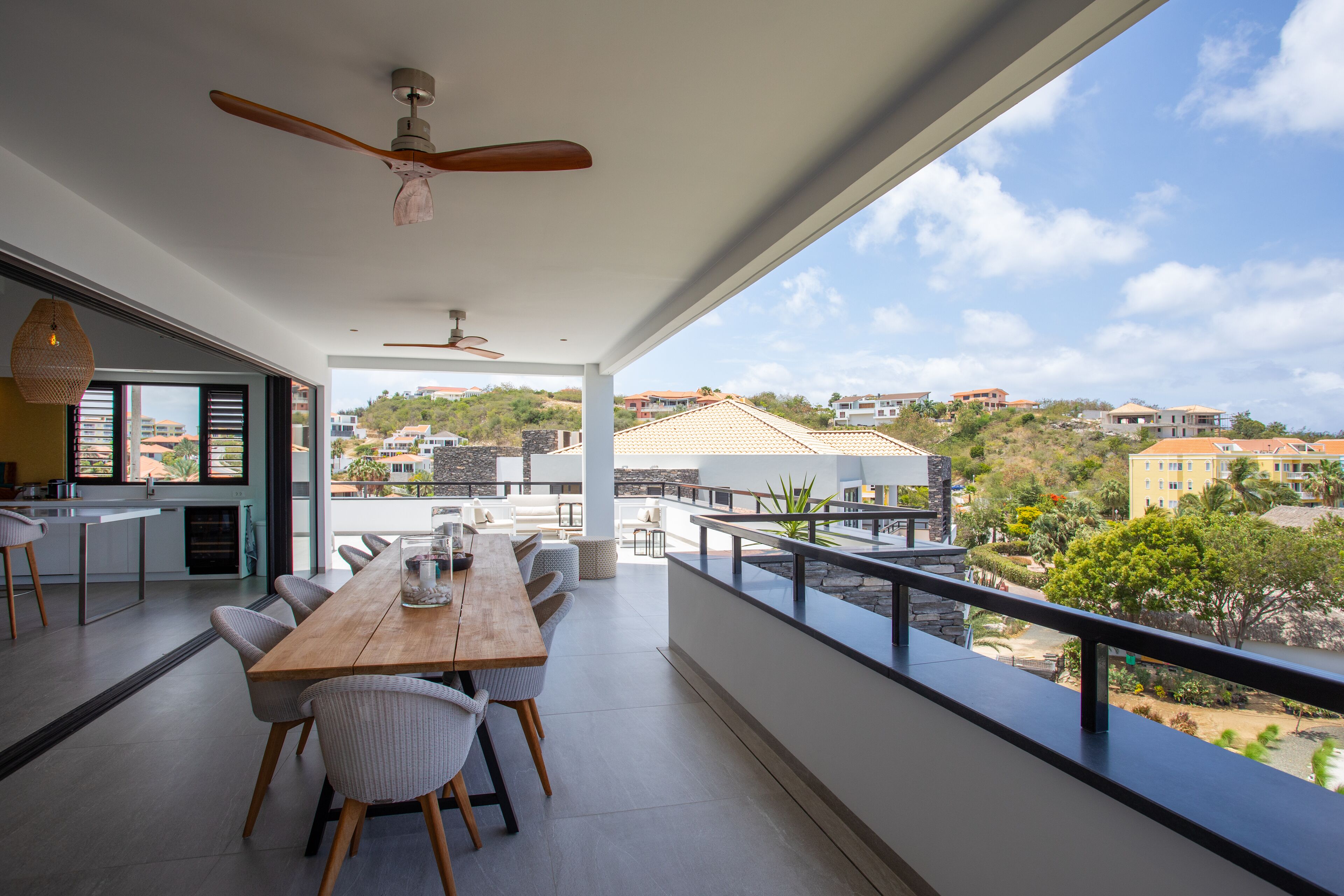 A modern dining area with a wooden table and chairs, a ceiling fan, and a view of the surrounding neighborhood.