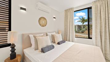 Habitación de hotel con una cama grande, dos lámparas de noche, aire acondicionado instalado en la pared y vista a palmeras a través de la ventana.