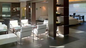 Een moderne hotel lobby met een receptiebalie, een zithoek en een groot raam dat natuurlijk licht binnenlaat.