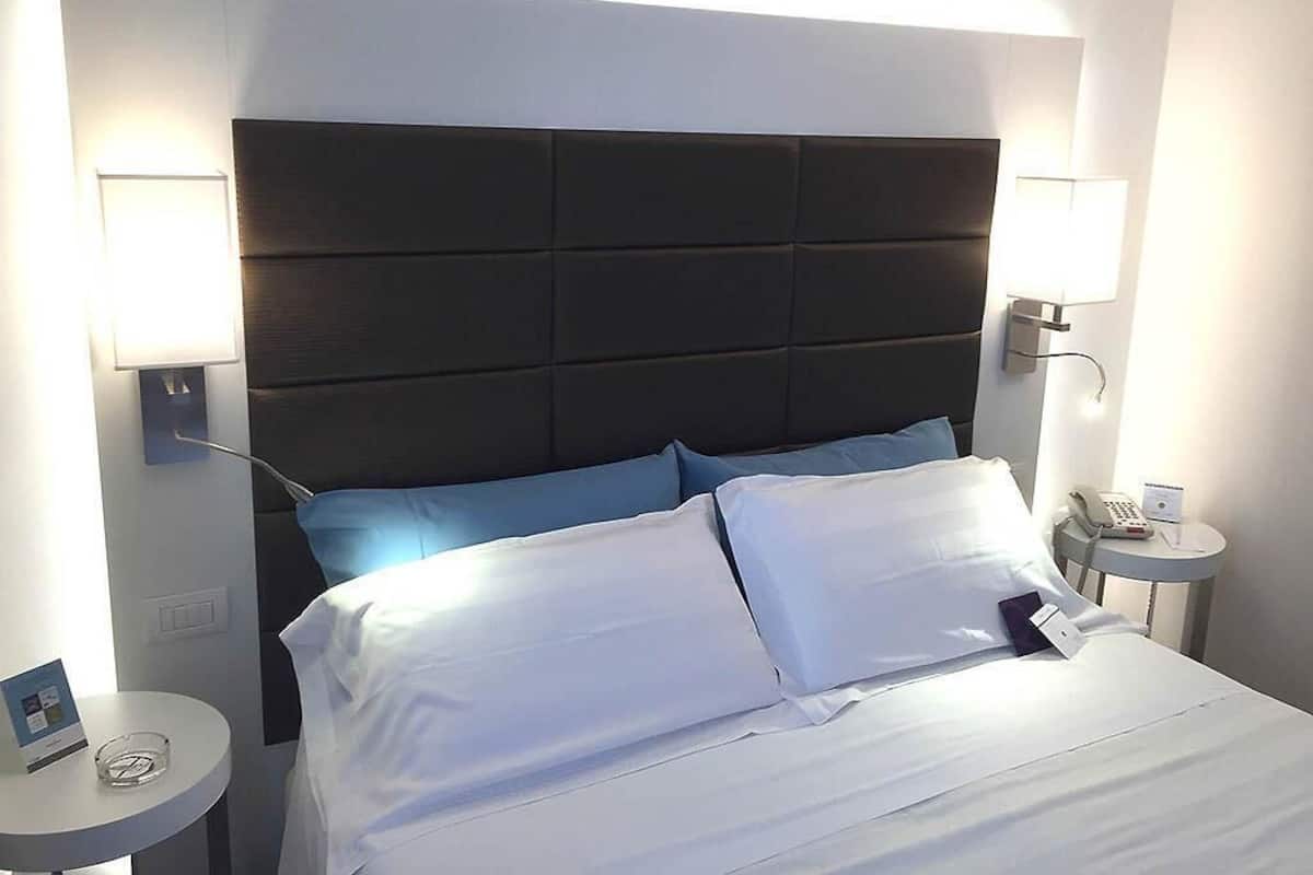 Una habitación de hotel con una cama grande, dos mesitas de noche y un cabecero moderno.