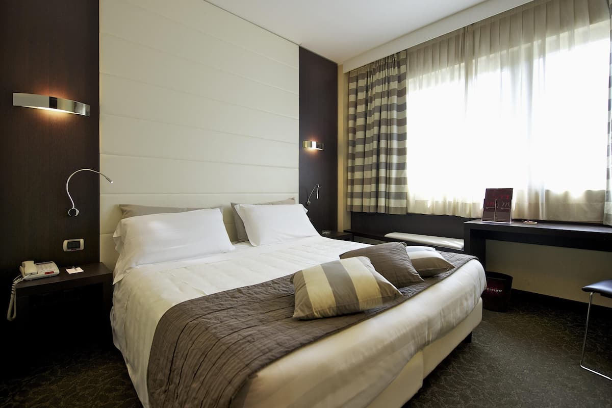 Una habitación de hotel con una cama grande, mesitas de noche, un escritorio y una ventana con cortinas.