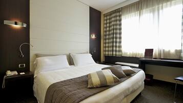 A hotel room with a large bed, bedside tables, a desk, and a window with curtains.