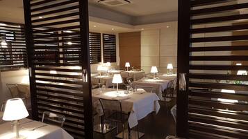 A modern dining area with tables set for service, overhead lighting, and a partition with horizontal slats.