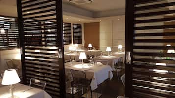A modern dining area with tables set for service, overhead lighting, and a partition with horizontal slats.