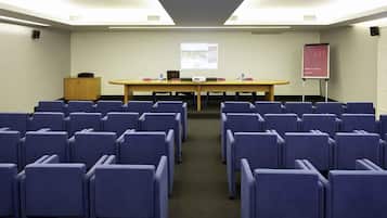 A conference room with rows of chairs, a long table, a projector screen, and a presentation stand.