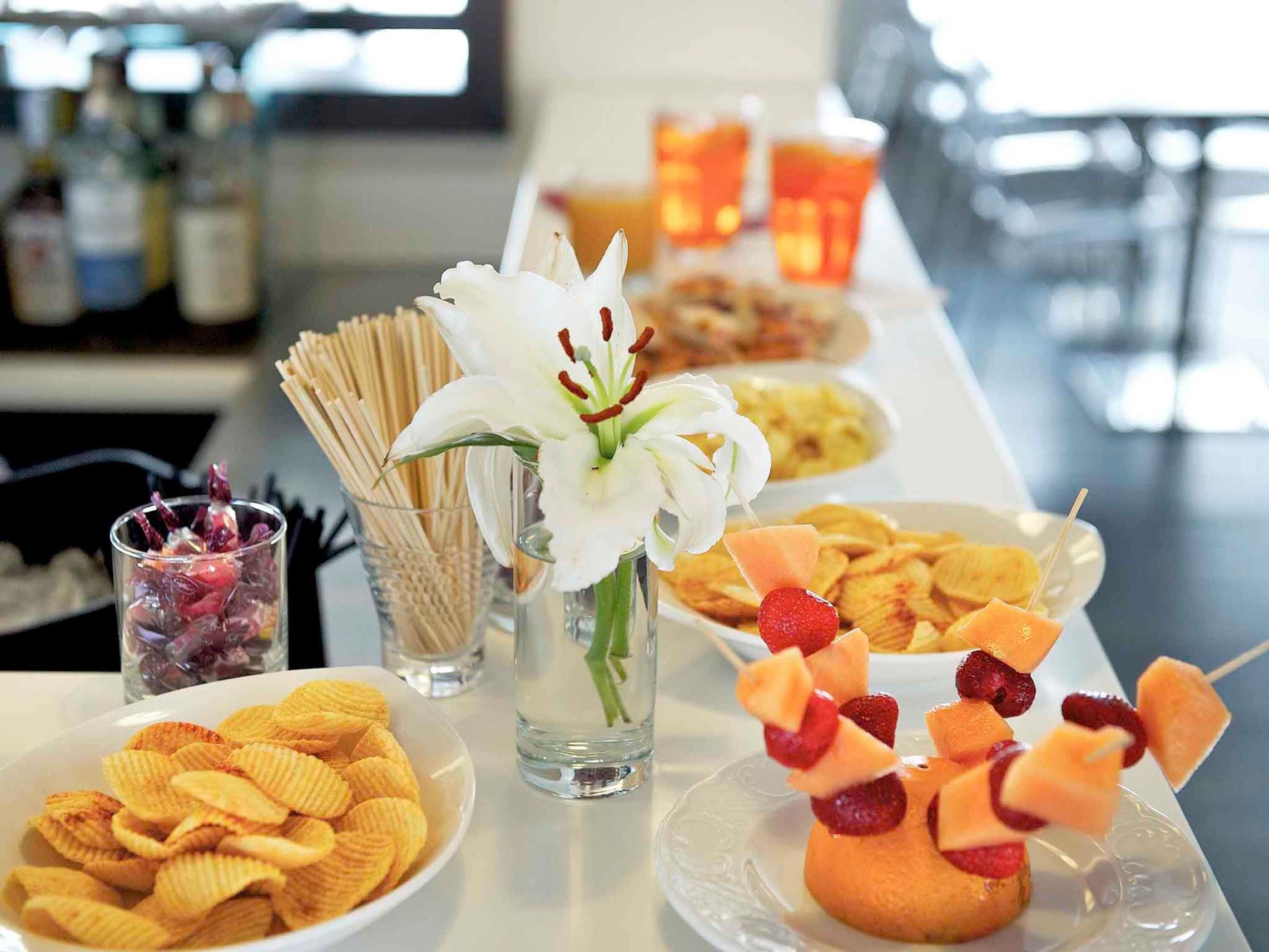 A buffet table with various food items, including chips, fruit skewers, and a white flower in a vase.