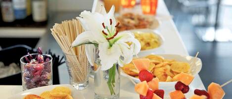 A buffet table with various food items, including chips, fruit skewers, and a white flower in a vase.
