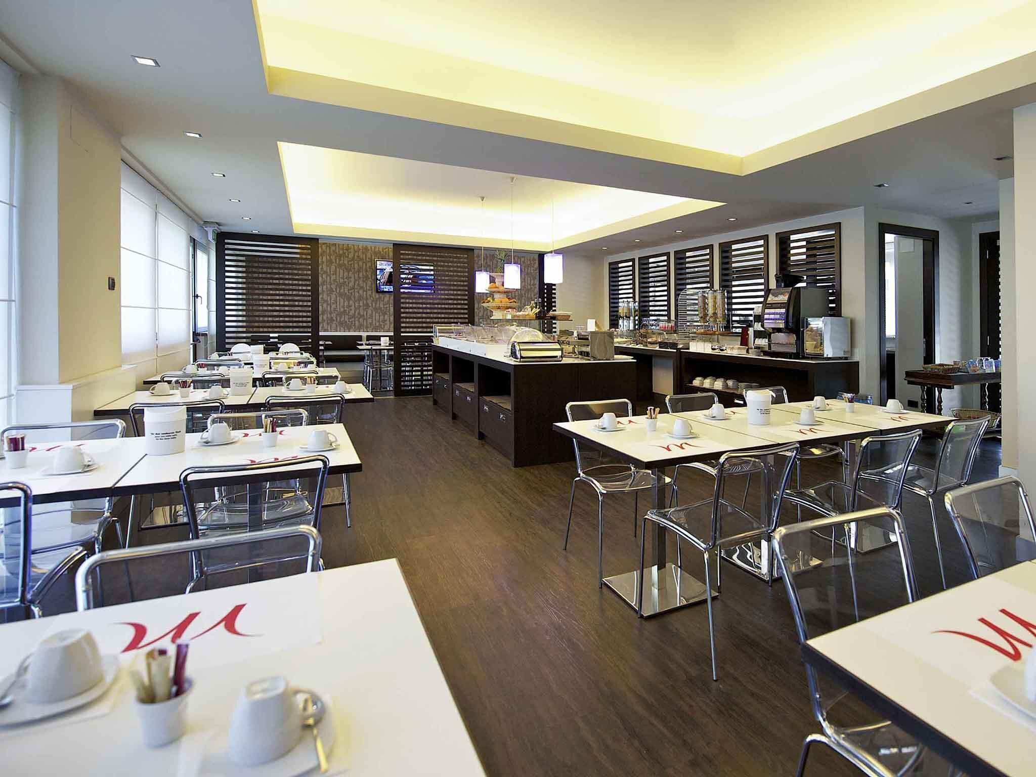 A modern restaurant with multiple tables, chairs, and a central bar area.