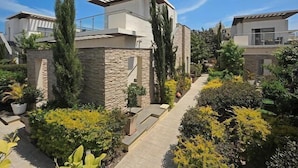 A modern residential building with a stone facade, a sloped roof, and a garden with various plants and shrubs. - E Hotel Spa & Resort Cyprus (Pervolia)