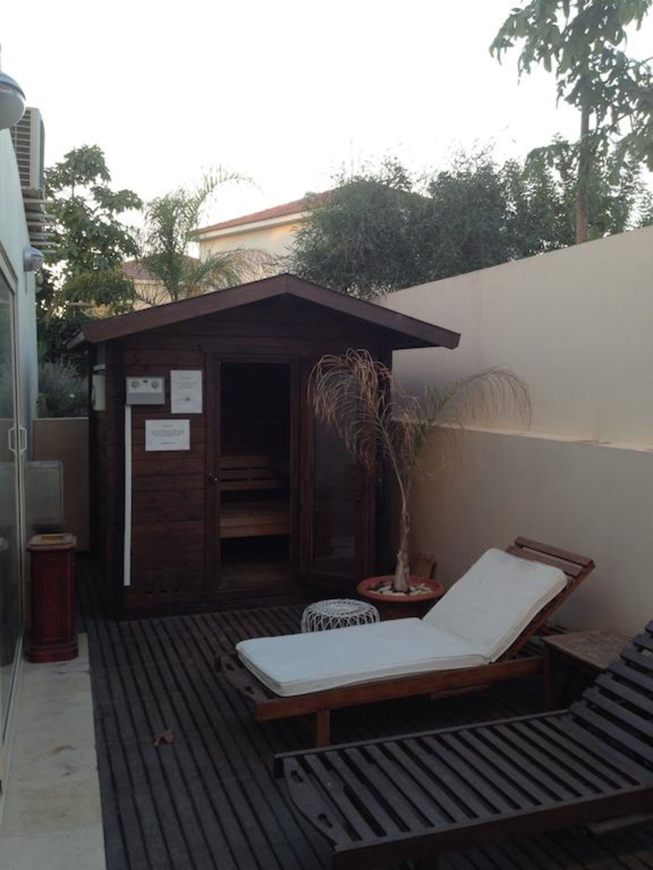 Een houten terras met een enkele lounge fauteuil en een klein houten constructie met een deur.