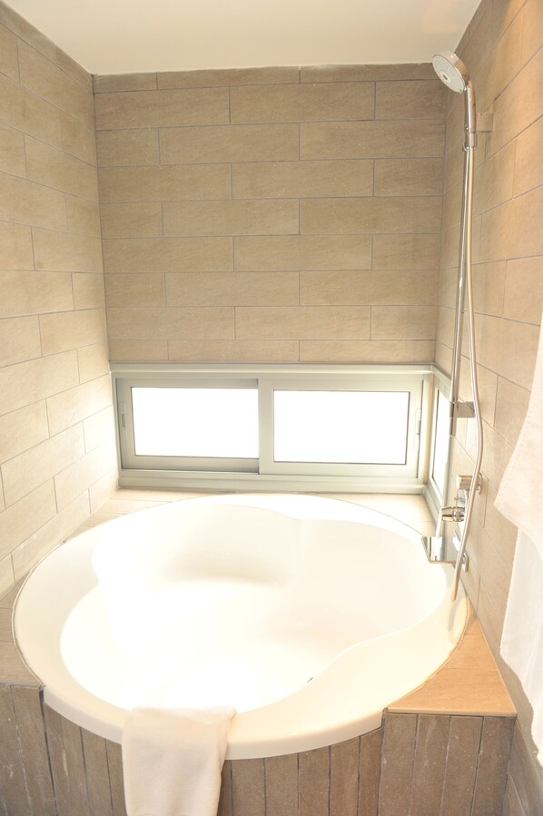 Un baño con una bañera grande, una ventana y una ducha.