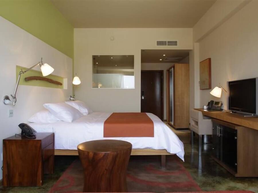 Een hotelkamer met een bed, nachtkastje, lamp, televisie en een klein houten krukje.