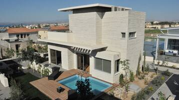 Une maison moderne à deux étages, dotée d’une piscine, de grandes fenêtres et offrant une vue sur la mer.