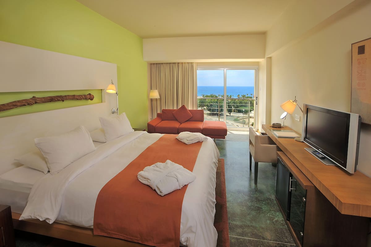 Habitación de hotel con cama, sofá, televisión y balcón con vista al mar.