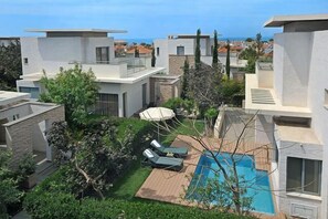 A modern residential complex with a swimming pool, lounge chairs, and a view of the sea.