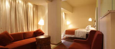 Ein Hotelzimmer mit einem roten Sofa, einem Holztischchen, einem Bett mit weißer Bettwäsche und zwei Nachttischlampen.