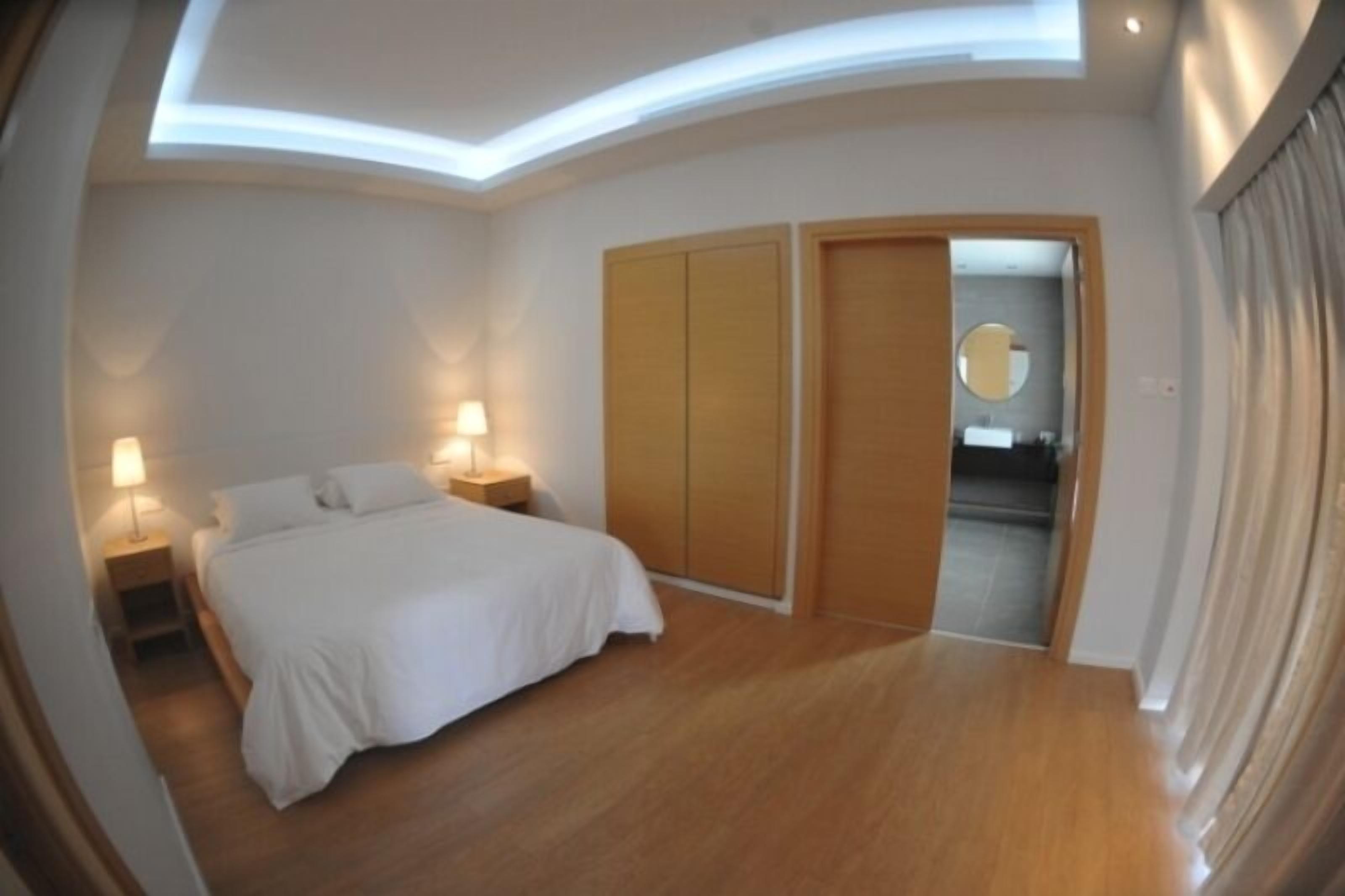 Quarto com cama, abajures, guarda-roupa e um espelho redondo.