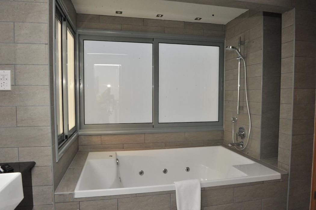 Et moderne badeværelse med et stort badekar, en bruser og et vindue med matterede glas.