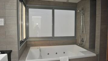 Une salle de bain moderne dotée d’une grande baignoire, d’une douche et d’une fenêtre avec des panneaux en verre dépoli.