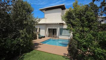 Una casa moderna con piscina, un porche cubierto y un césped bien cuidado.