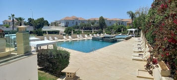 Una piscina al aire libre, sombrillas, sillones reclinables de piscina