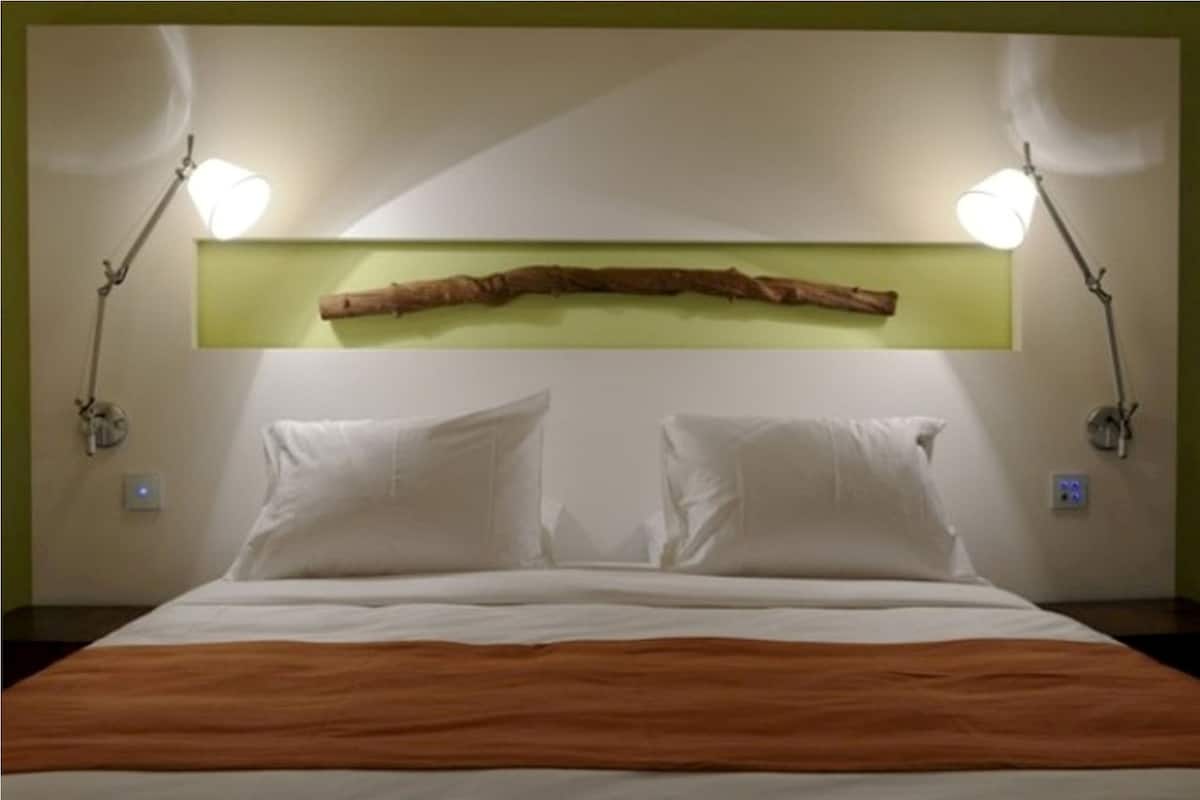 Una cama con sábanas blancas y cabecera de madera, flanqueada por dos lámparas de pared.