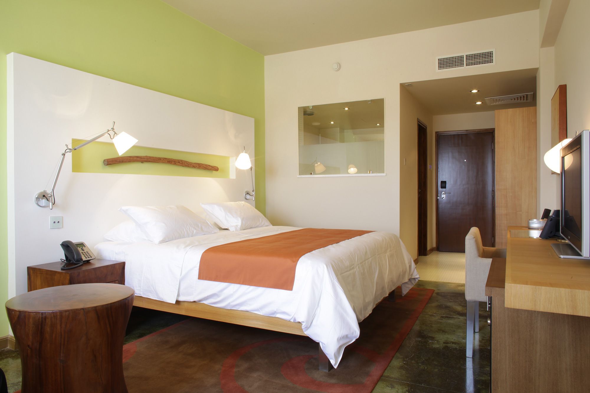 Habitación de hotel con cama, mesita de noche, lámpara y escritorio con silla.
