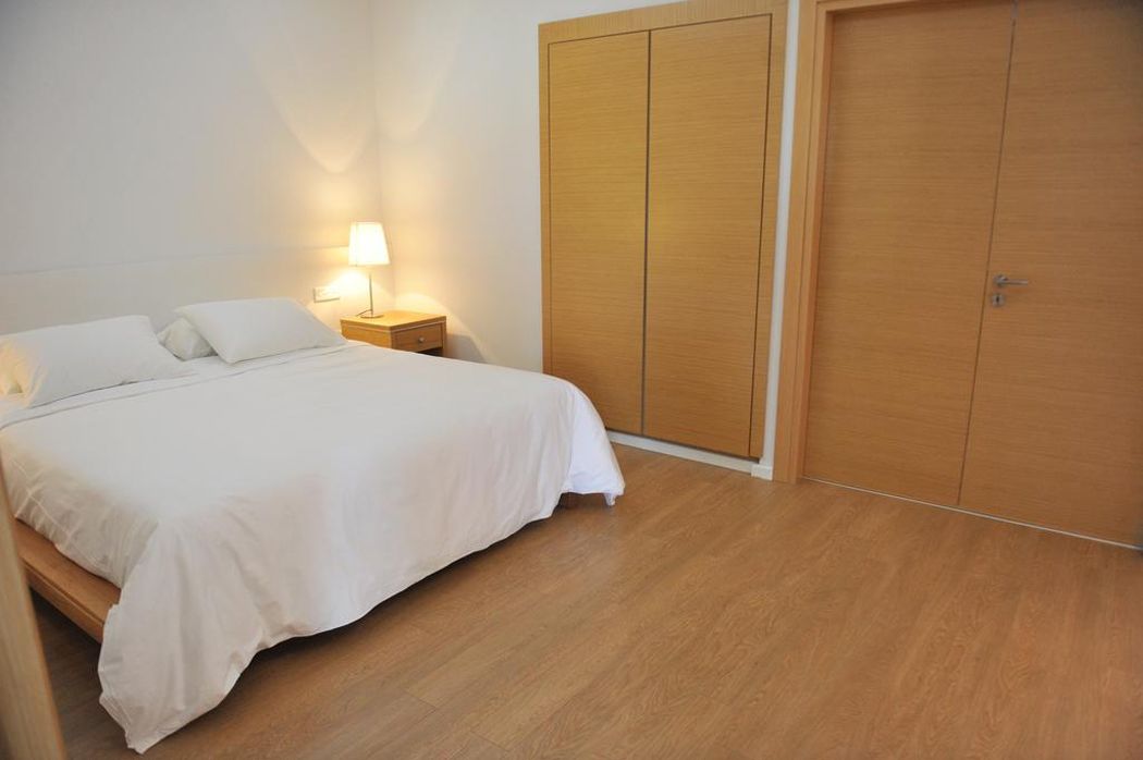Un dormitorio con una cama, una mesita de noche con lámpara y un armario de madera.