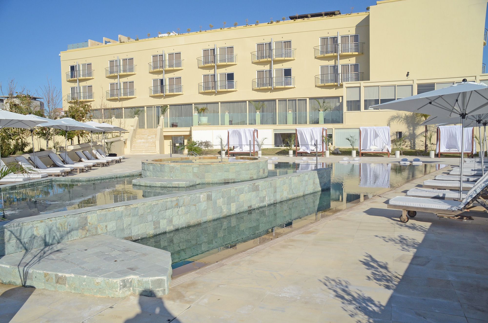 A hotel with a swimming pool, sun loungers, and a covered seating area.