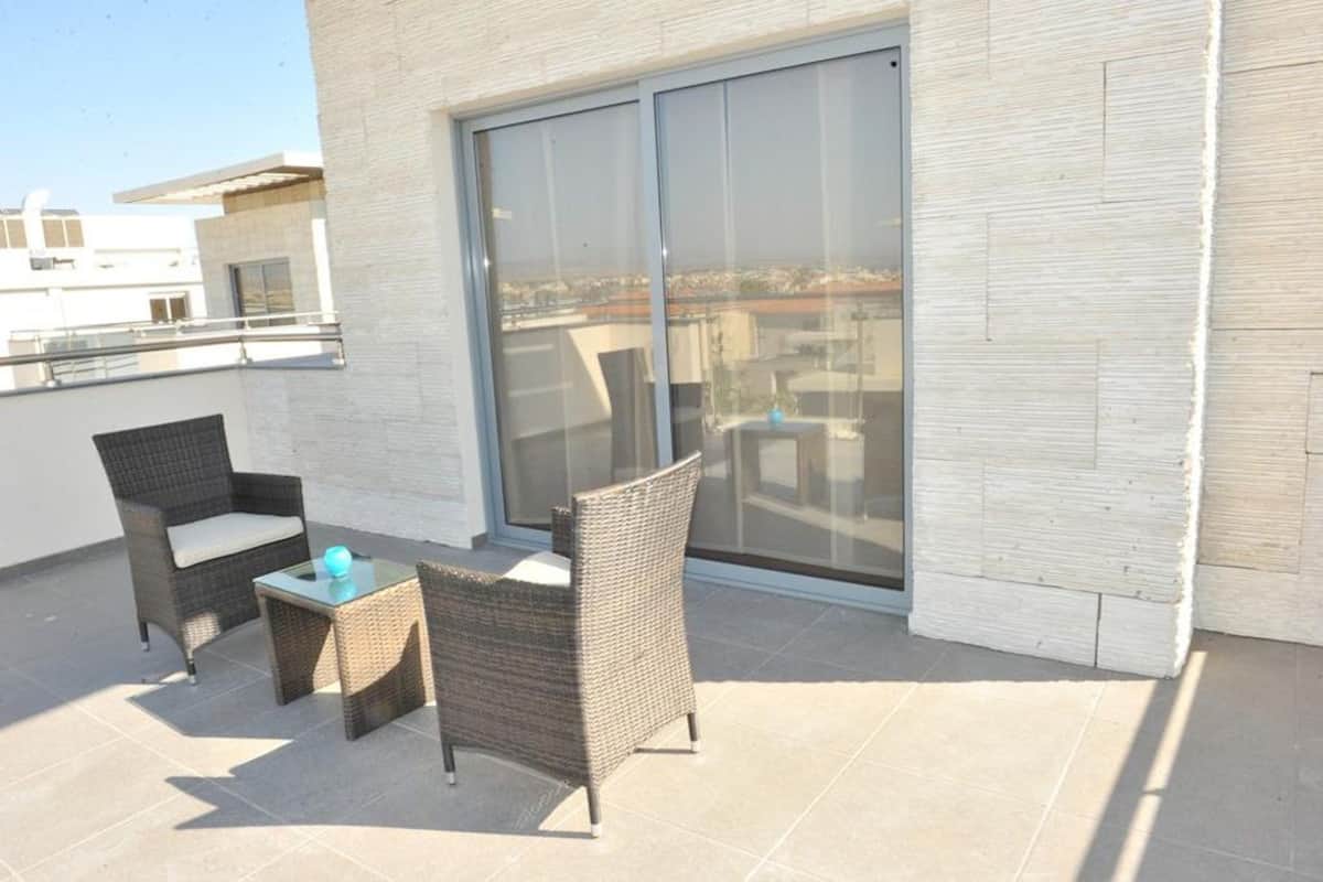 Un balcón con mobiliario de mimbre y una puerta de cristal.