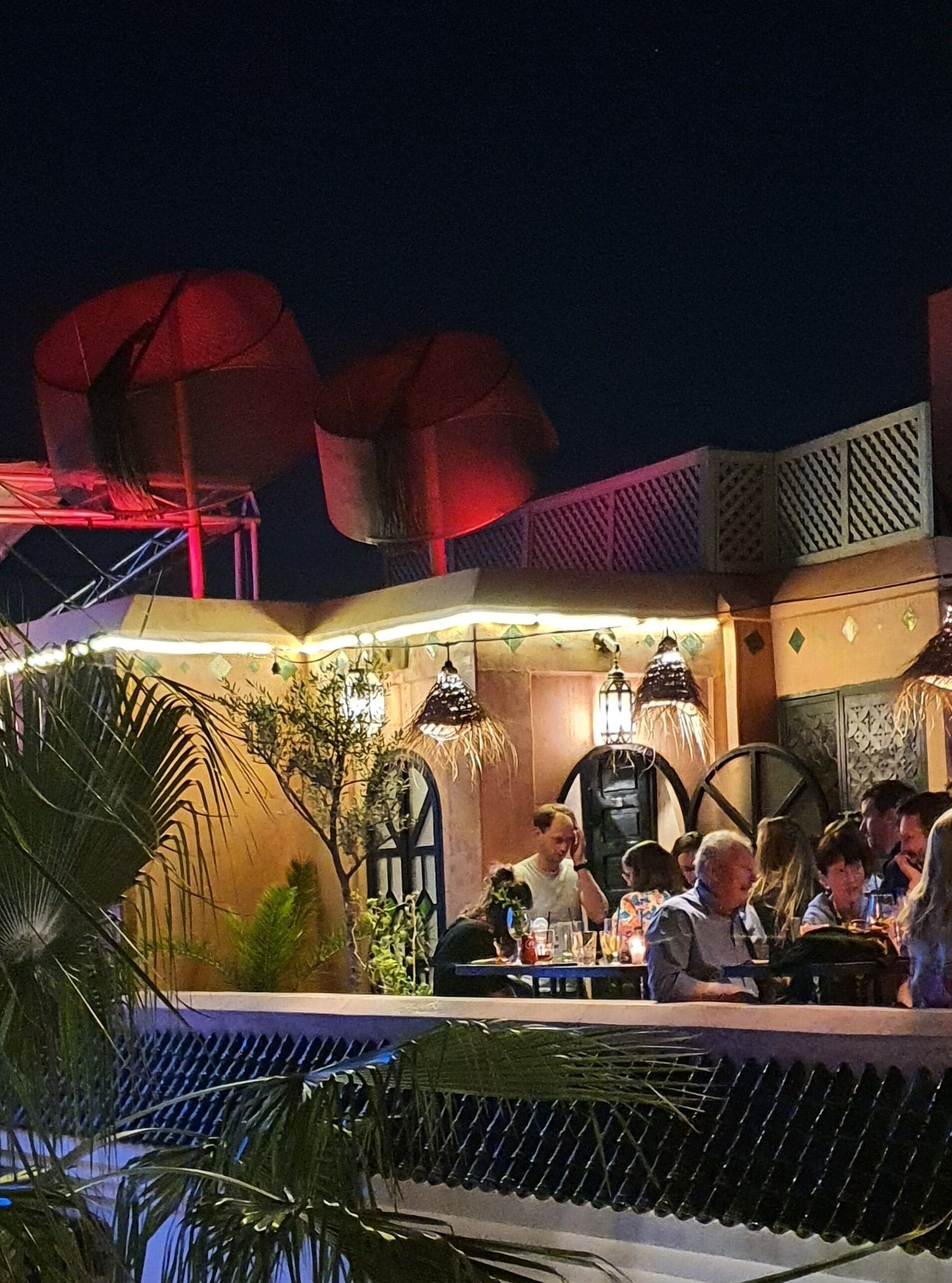 Un espacio de comedor al aire libre con mesas y sillas, rodeado de plantas tropicales y sombrillas decorativas.