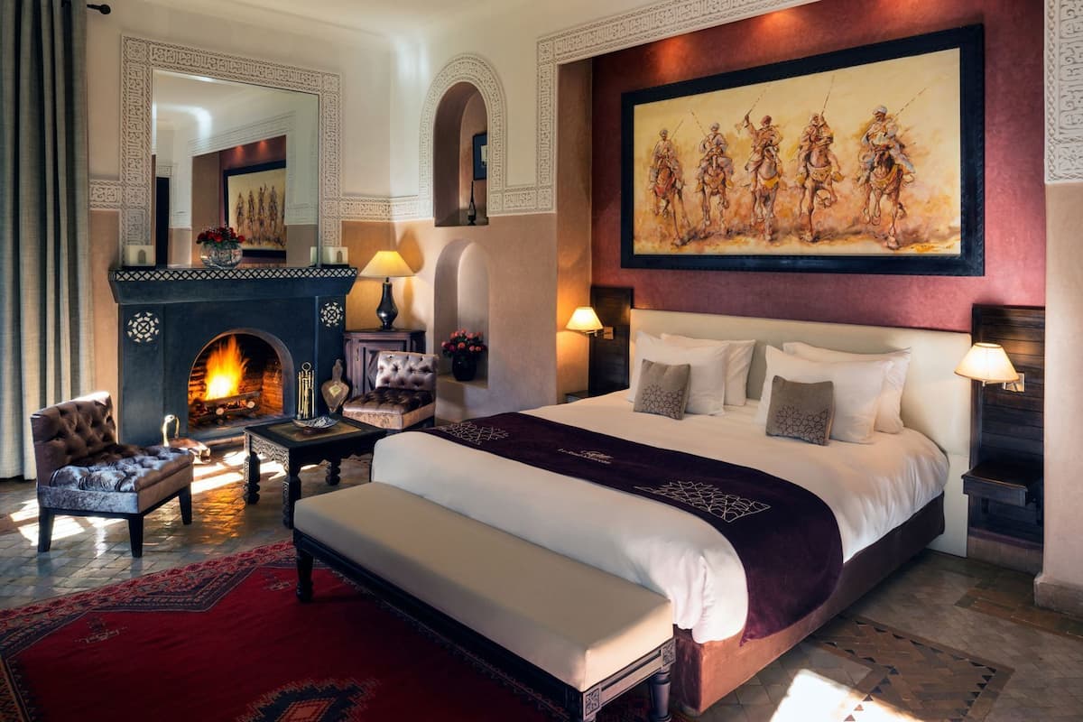 A large bed with a headboard, a fireplace, a painting, and a red carpet.