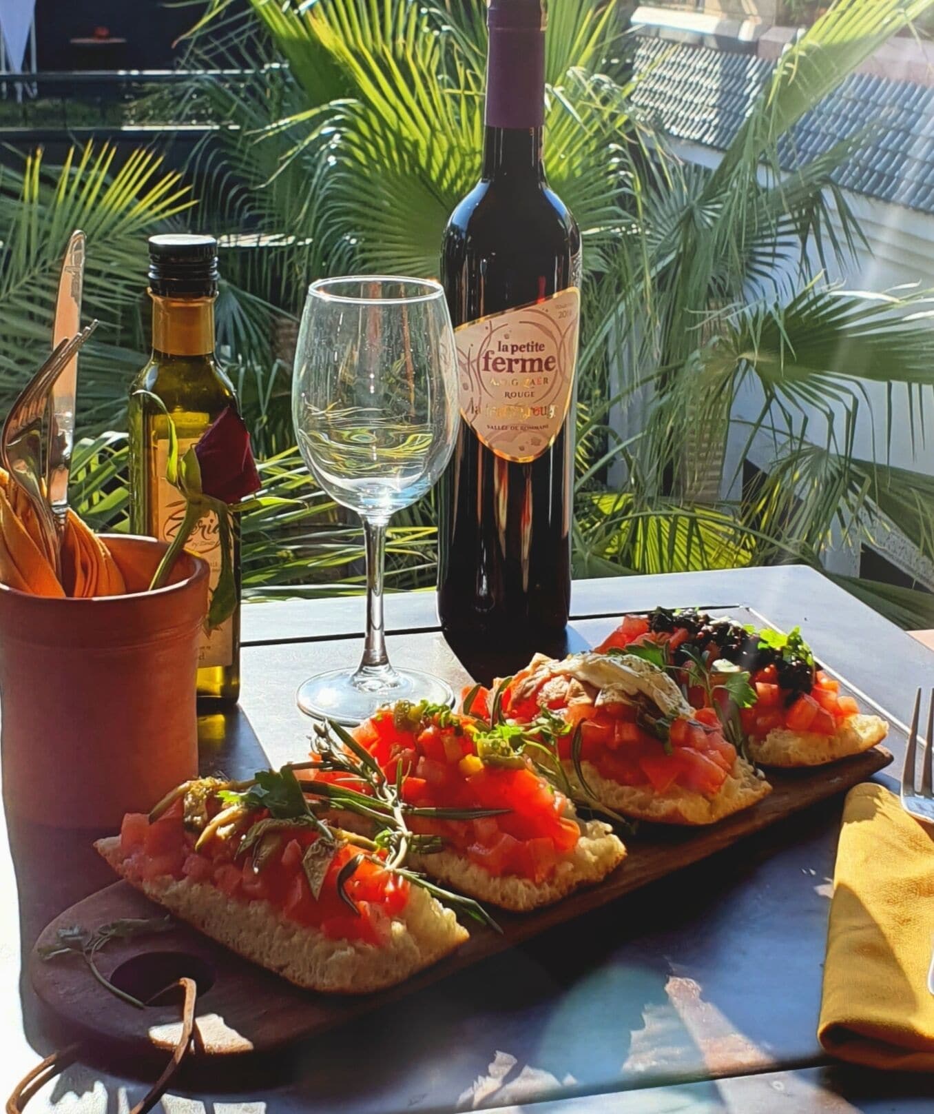 Een tafel met een fles wijn, een glas en drie stukken bruschetta op een houten plank.